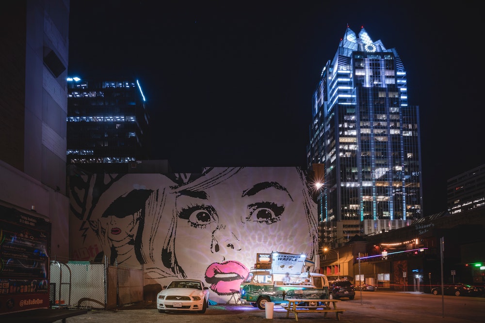 A photo of a comic-book-art style wall mural in Austin at night, with a food truck parked in the foreground