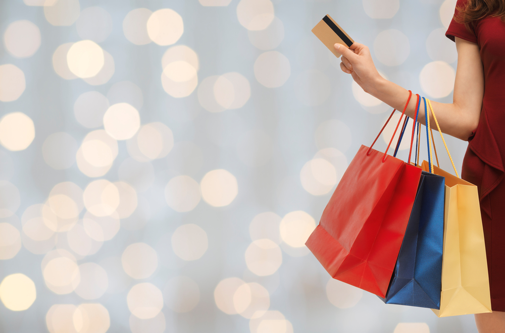 people, sale and consumerism concept - close up of woman with shopping bags and bank or credit card over holidays lights background